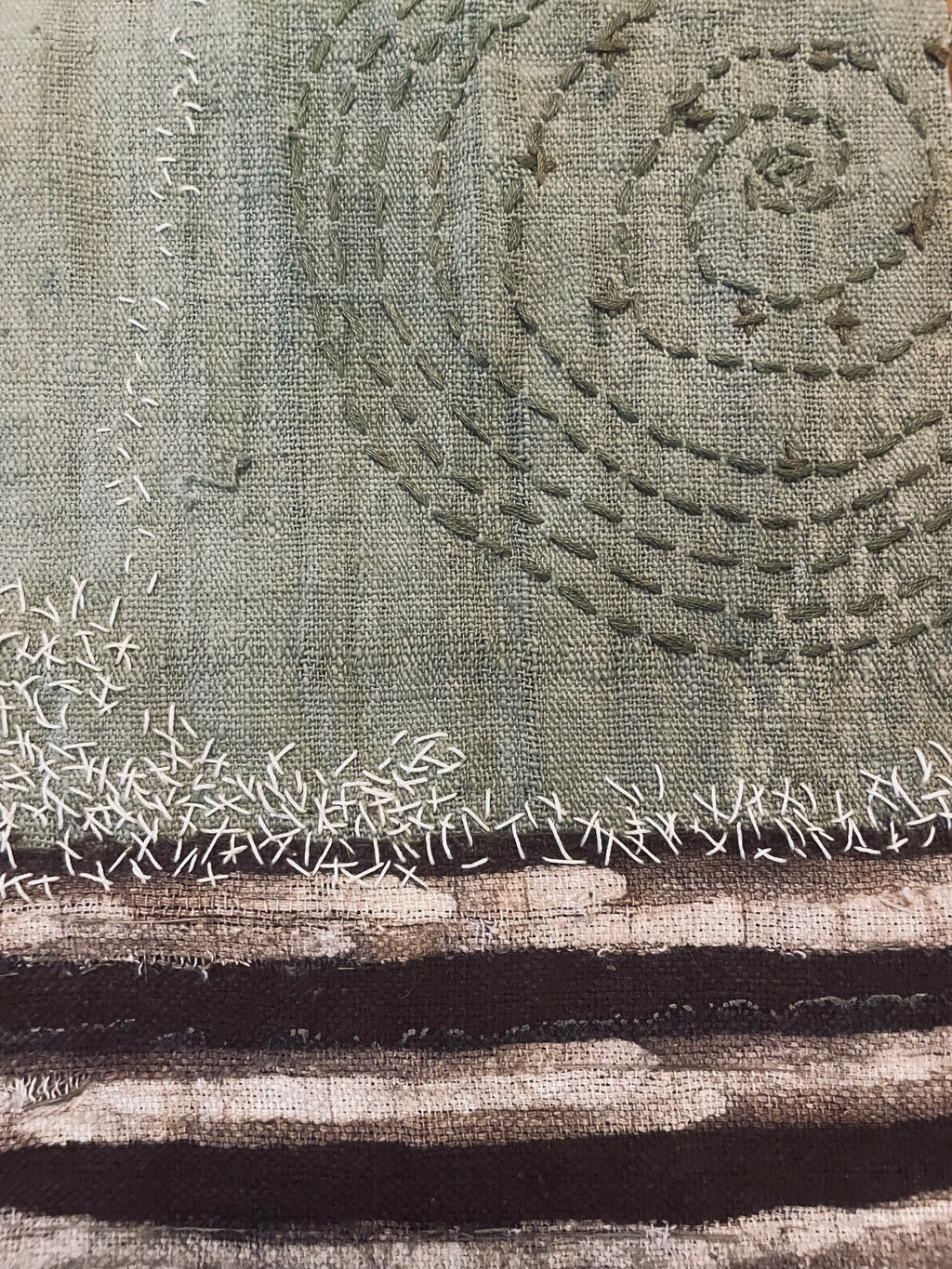 Textile art piece with concentric circle pattern and embroidered details on a textured fabric background.